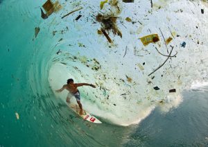 surfer riding in a wave full of plastic